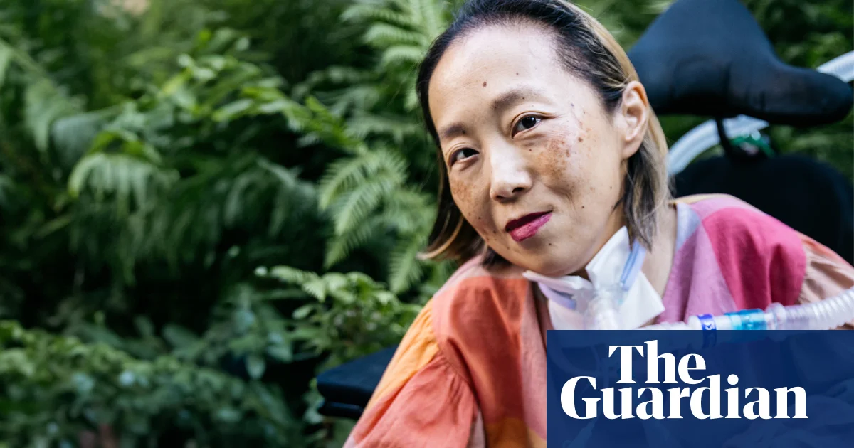 Portrait of Alice Wong, a disability activist and MacArthur genius, sitting outdoors surrounded by lush green foliage. She is wearing a colorful outfit, and a ventilator tube is visible at her neck. Her expression is calm and contemplative, reflecting her resilience and strength.