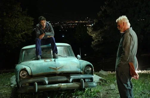 Still from Peaceful Warrior. Dan sits atop an old beat up car looking pensive. His mentor, Socrates, looks on with his had down.