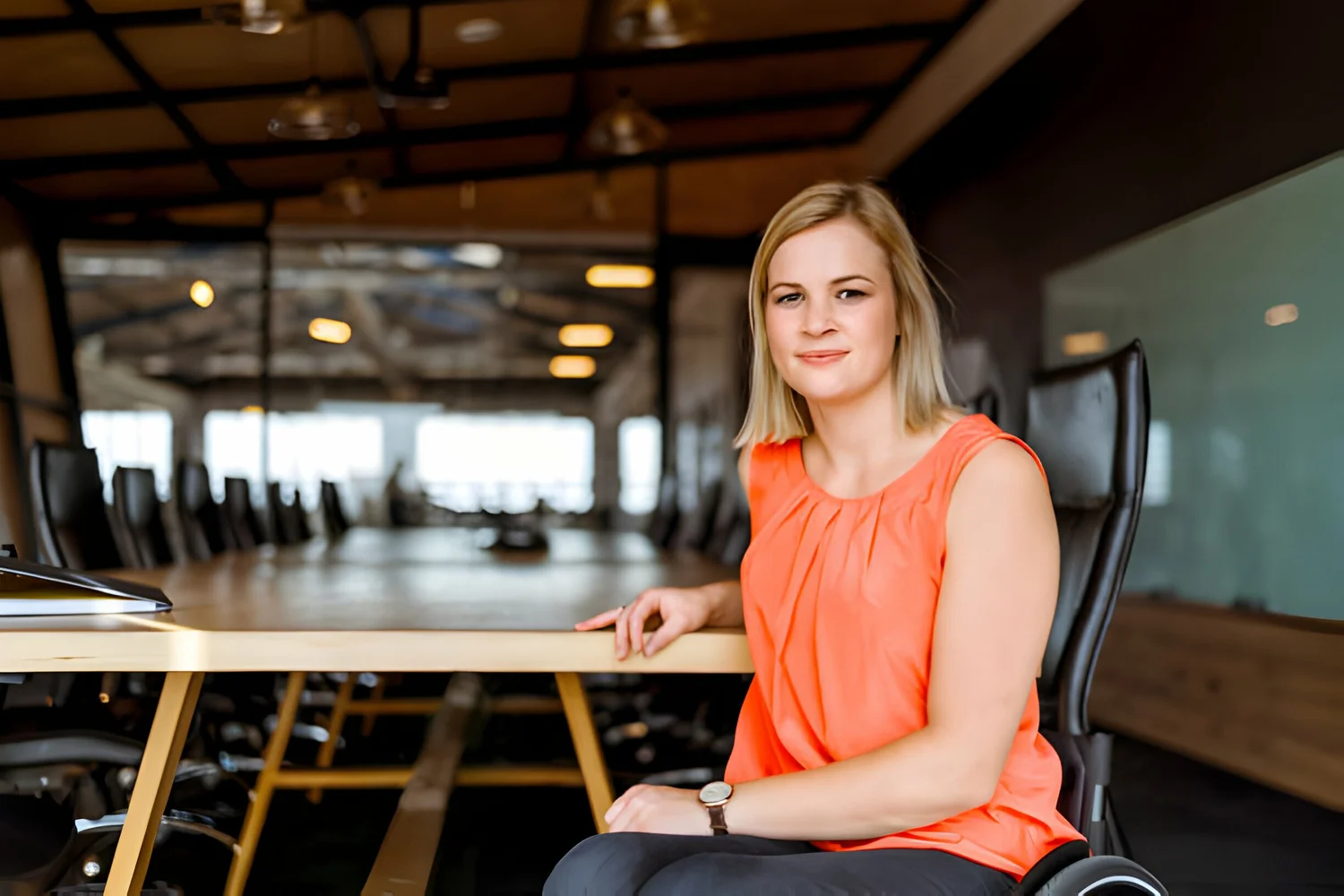 A photo of confident businesswoman sitting on wheelchair. Portrait of confident female professional is in board room. She is in smart casuals at creative office.