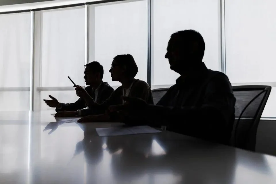 A silhouette of three people sitting in a boardroom.