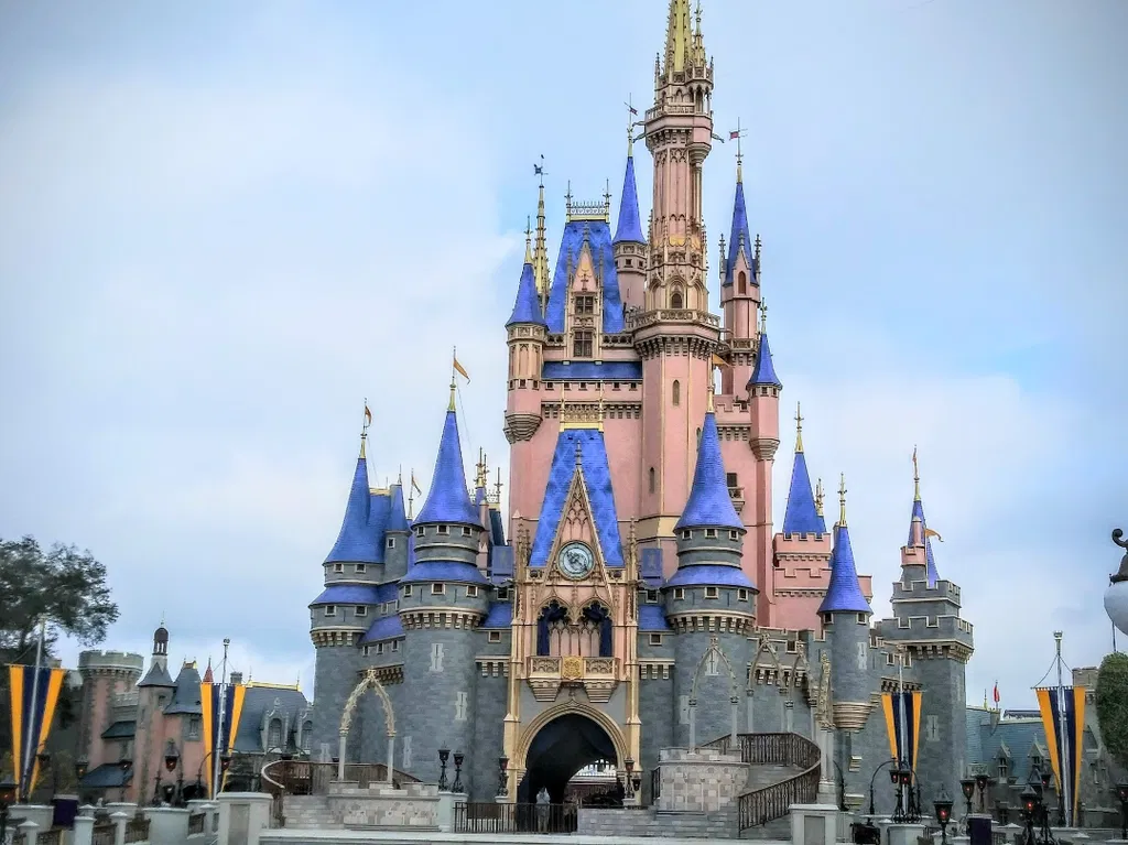 Cinderella Castle at Walt Disney World in Florida, a majestic and iconic fairytale castle with blue rooftops, golden spires, and pink and gray walls. The setting includes a clear sky and a few decorations in the foreground, emphasizing the grandeur and magical atmosphere of the castle.