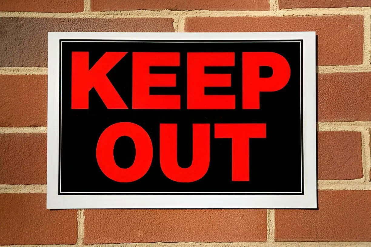 “Keep Out” Sign in red lettering against a brick wall.